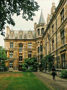 a person walking down a sidewalk in front of an old building with many windows and towers