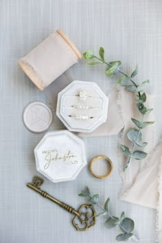 an assortment of wedding rings, ring box and napkins on a table with greenery