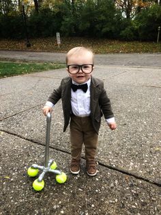 a little boy with glasses and a bow tie standing next to tennis balls on the ground