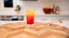 an orange and red drink sitting on top of a wooden table next to a kitchen counter