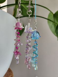 three different colored glass beads hanging from a hook on a plant in front of a white wall