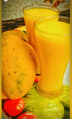 two glasses filled with orange juice next to some fruits and vegetables on a tablecloth