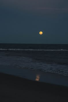 the full moon is setting over the ocean