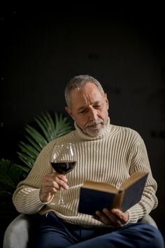 an older man is reading a book and holding a glass of wine