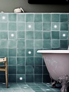 a chair sitting next to a bath tub in a bathroom with green tiles on the walls