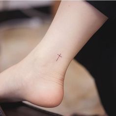 a small cross tattoo on the foot of a woman's right foot, with her left leg visible