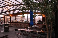 an outdoor patio with tables and chairs under a roof over looking the city at dusk