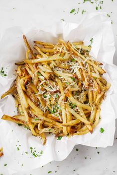 french fries with parmesan cheese and herbs in a white paper bag on a table