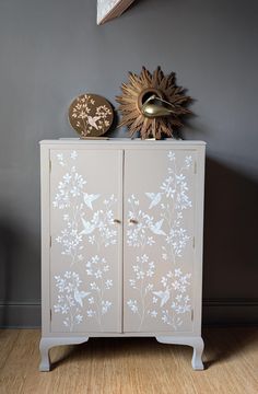 a white cabinet with flowers painted on the front and bottom, against a gray wall