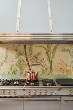 a stove top oven sitting next to a wall with plants painted on the back splash