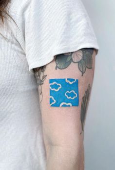 a woman's arm with a blue and white cloud tattoo on her left arm