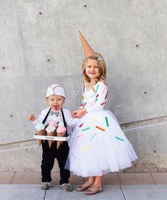 two children dressed up in costumes standing next to each other on the side of a building