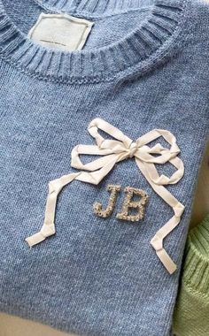 two sweaters with bows on them and the letters jb are made out of yarn