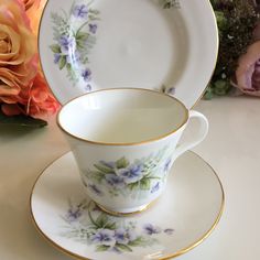 a cup and saucer sitting on top of a table next to a bouquet of flowers