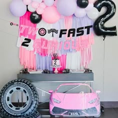 a pink car is parked in front of balloons and streamers that spell out the number two