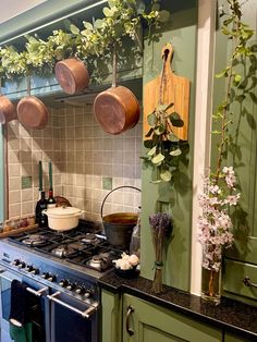 pots and pans are hanging on the wall above an oven in a green kitchen