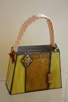 a yellow and brown purse hanging from a wall with a red ribbon on the handle