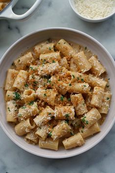 a white bowl filled with pasta next to two bowls of cheese and parmesan