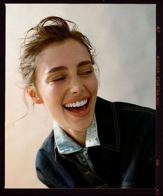 a woman smiling with her eyes closed and hair blowing in the wind while wearing a denim jacket