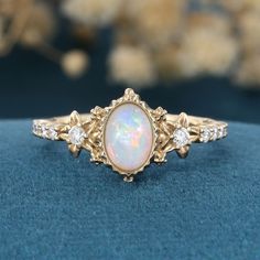 an opal and diamond ring sits on a blue velvet surface in front of some flowers