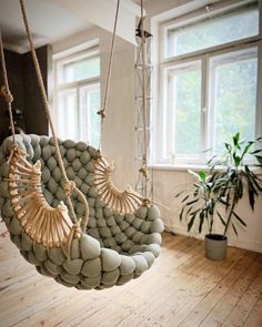 a hanging chair made out of rocks in a room with wooden floors and large windows