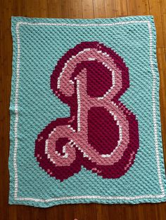 a crocheted blanket with the letter b on it and a hand holding a knitted object