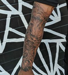 a man with a dragon tattoo on his arm and leg is standing in front of a black brick wall