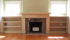 an empty living room with wood floors and built - in bookshelves on either side of the fireplace