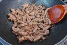 meat is being cooked in a frying pan with a wooden spoon on the side