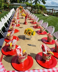 a long table is set up with red plates and white chairs for an outdoor dinner