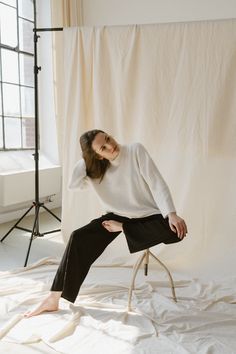 a woman sitting on top of a chair in front of a white backdrop wearing black pants