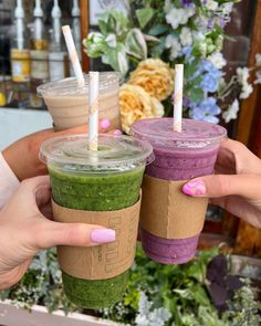 two people holding up cups with smoothies in them