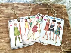 three tags with different styles of dresses hanging from strings on a piece of wooden plank