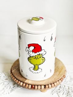 the grinch cookie jar is sitting on top of a wooden coaster and has a santa hat on it