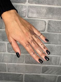 a woman's hand with black nail polish and tattoos on her left hand, next to a brick wall