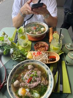 a person sitting at a table with bowls of food on it and a cell phone