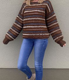 a woman standing in front of a wall wearing jeans and a sweater