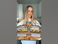 a woman is holding three trays of food