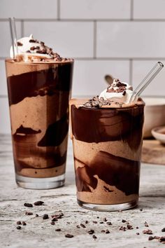 two glasses filled with chocolate milkshakes sitting on top of a counter next to each other