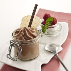 two desserts in small glass jars on a plate with spoons and raspberries