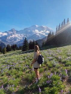 a woman with a backpack is walking through the grass and wildflowers in the mountains