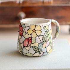 a stained glass coffee cup sitting on top of a white counter next to a wooden dresser