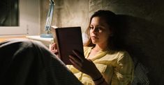 a woman is reading a book while sitting on a bed with her feet propped up against the wall