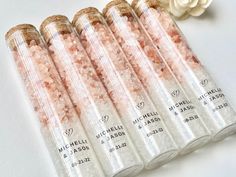 five tubes filled with pink salt next to a white flower