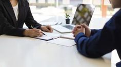 two people sitting at a table with laptops and papers in front of each other