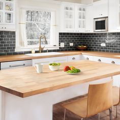 a kitchen with white cabinets and wooden counter tops, along with two bowls of vegetables on the island