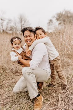 a man holding two children in his arms and smiling at the camera while standing in a field