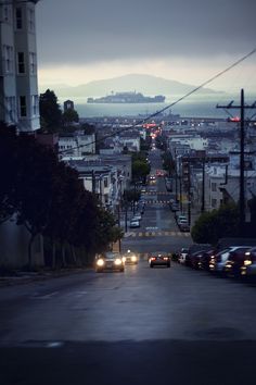 a city street at night with cars driving down the road and an overcast sky