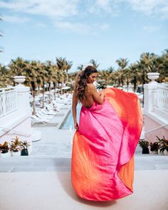 a woman in an orange and pink dress is standing on a balcony with palm trees