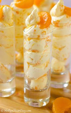 three glasses filled with dessert sitting on top of a wooden table next to an orange slice